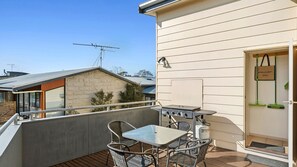 Un balcon avec une table et des chaises, un barbecue et une porte sur laquelle est apposée une plaque indiquant « APOLLO BAY 3233 ».