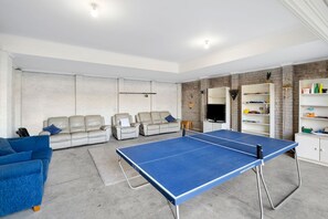 A room with a ping pong table, two sofas, a TV, and a bookshelf.