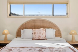 Een bed met een rieten hoofdbord, twee bedlampen en een raam erboven.