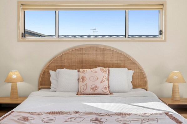 A bed with a rattan headboard, two bedside lamps, and a window above.