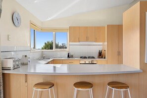 A modern kitchen with a large island, wooden cabinets, a built-in oven, and a window providing natural light.