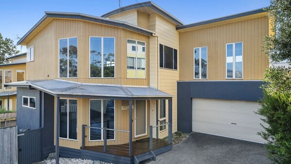 Une maison moderne à deux étages, dotée d’un porche abrité, de grandes fenêtres et d’un garage.