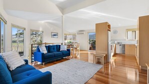 A spacious living area with a blue sofa, a dining table, and chairs. There is a kitchen area with a sink and cabinets. - Family Tides (Apollo Bay)