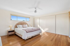 Ein Schlafzimmer mit Bett, Nachttischen, Deckenventilator, Fenster und Kleiderschrank.