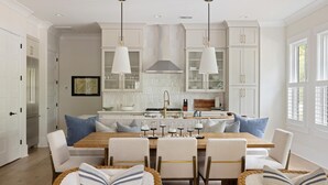 A modern kitchen with white cabinetry, a wooden dining table, and pendant lighting.