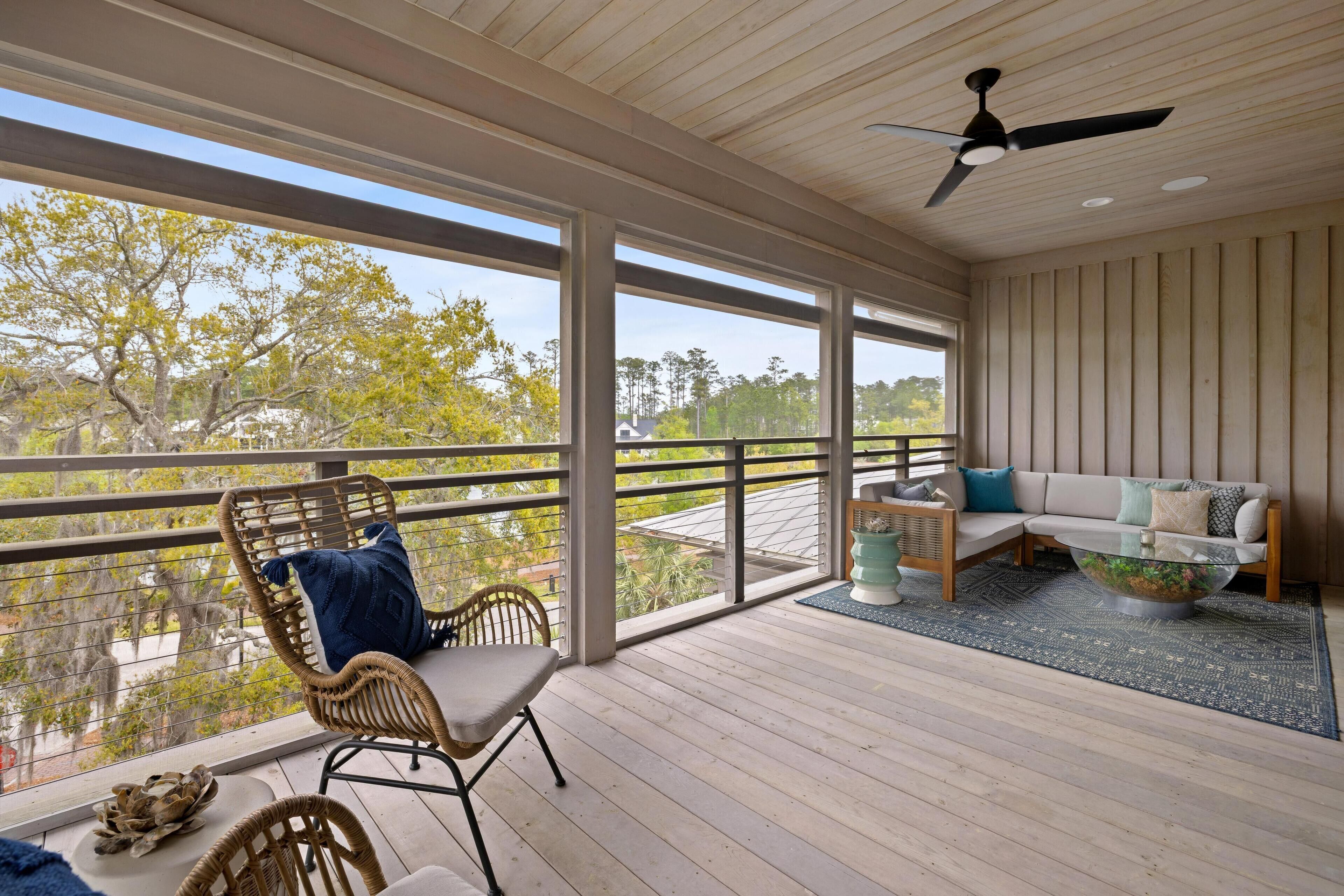 Ein geräumiger Balkon mit Holzboden, Deckenventilator, Korbstuhl, einer Couch mit Kissen und einem Glastisch.