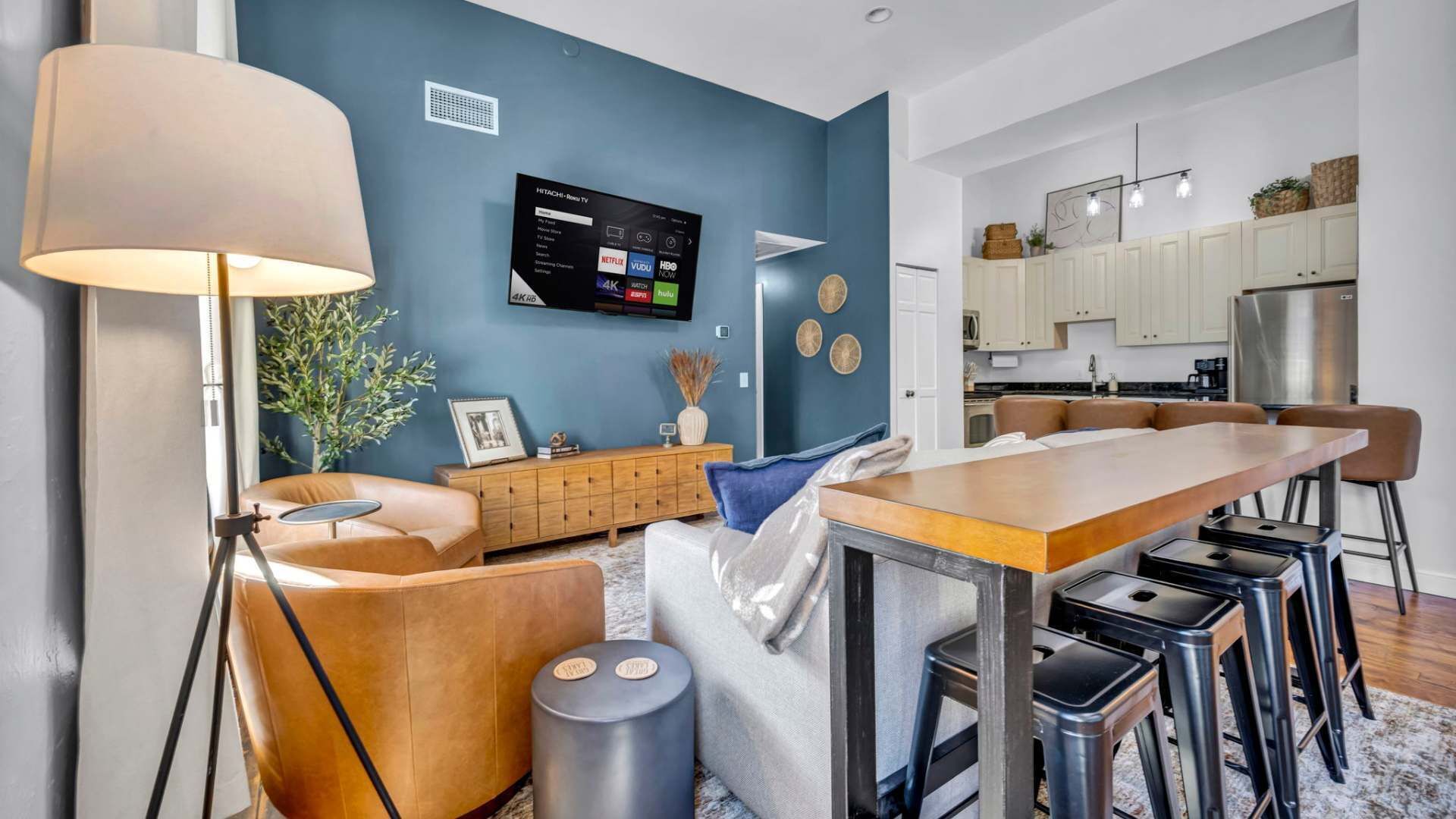A modern kitchen with a central island, bar stools, and a mounted TV displaying streaming services.