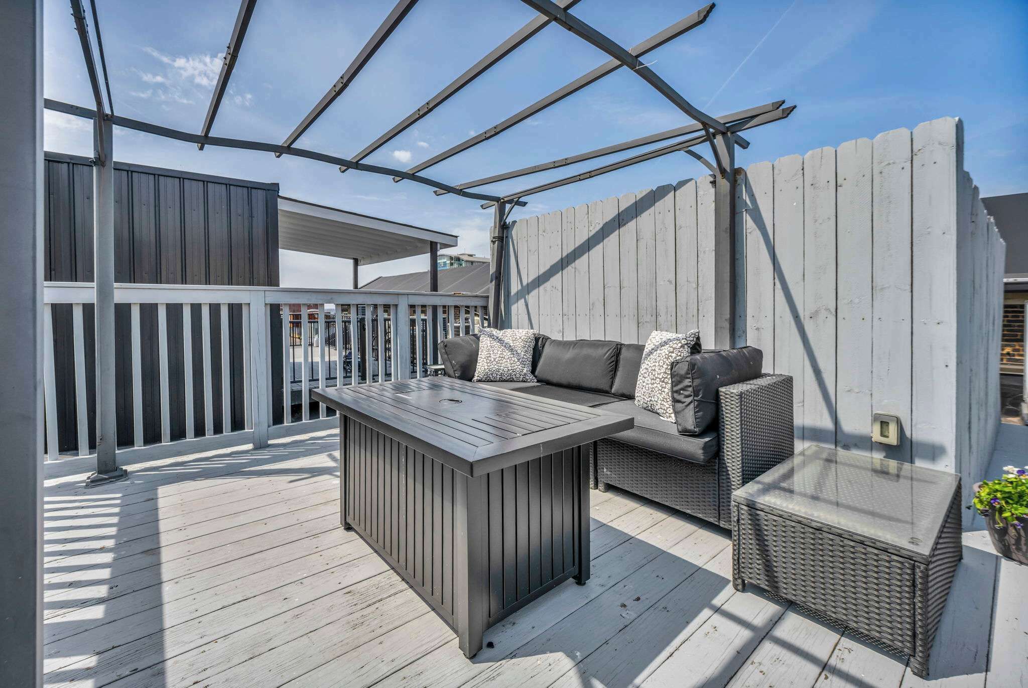 Une terrasse extérieure couverte, avec une table en bois, un banc rembourré et un canapé agrémenté de coussins.