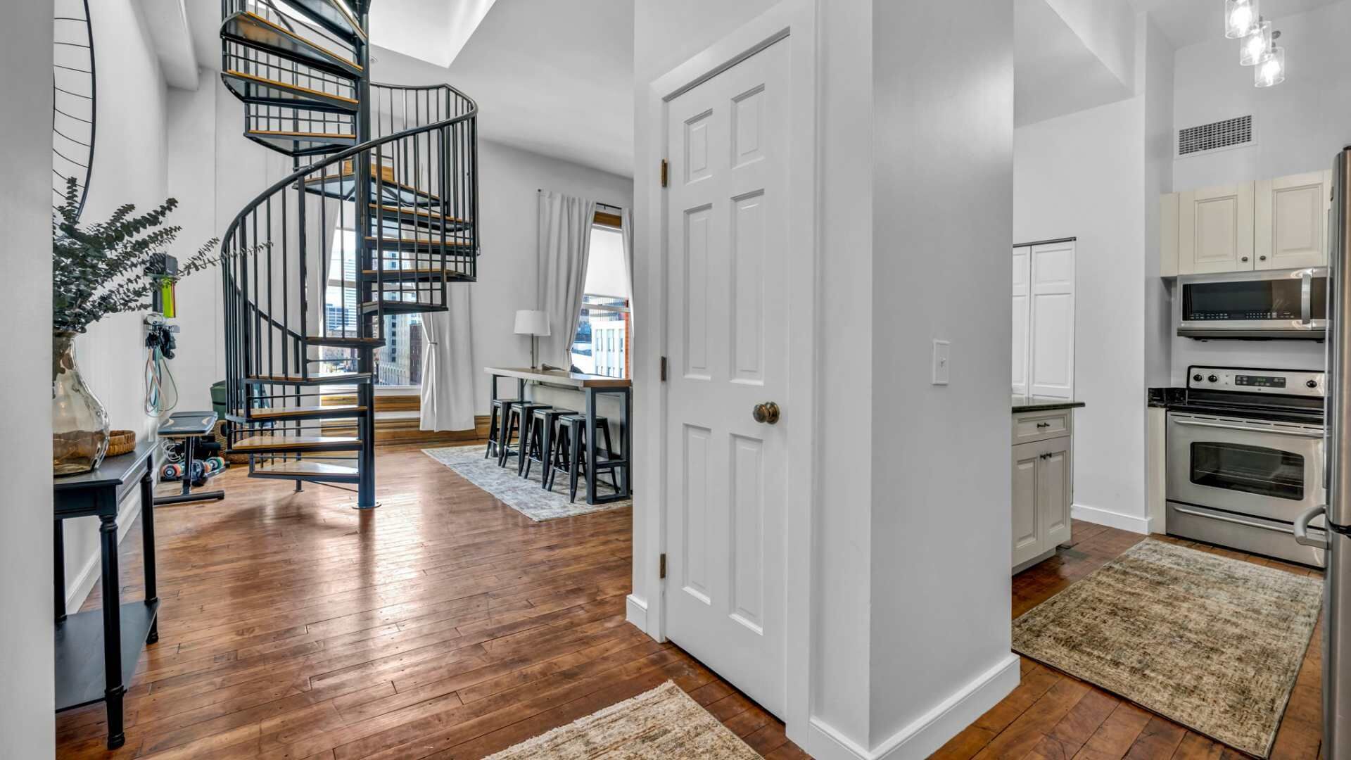 A modern kitchen with stainless steel appliances, a wooden floor, and a spiral staircase leading to an upper level.