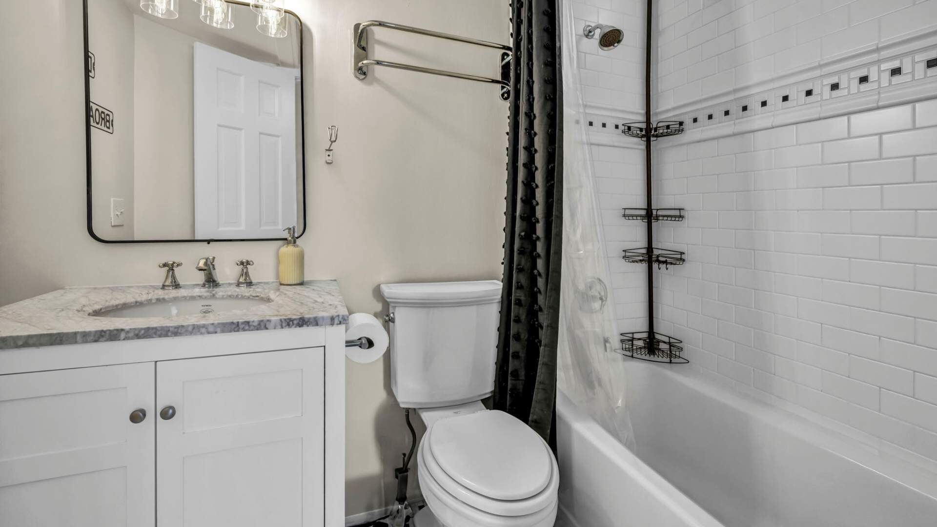 A bathroom with a white toilet, a sink with a marble countertop, a mirror, and a shower area with a black shower curtain.