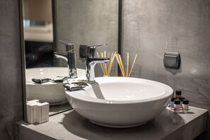 Ein modernes Badezimmer mit einem großen, weißen Waschbecken, einem Chromarmaturen und einem Spiegel. Auf der Ablage liegen Pflegeprodukte und ein Seifenspender.