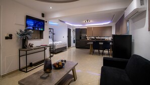 A modern living room with a flat-screen TV, a dining area, and a kitchen. - Black suites (Chania)