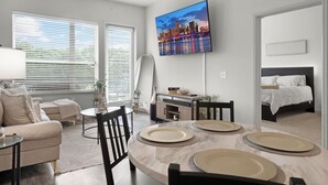 A modern living room with a dining area, a TV mounted on the wall, and a bed in the adjacent room. - Entire Unit Downtown Dallas, Texas - City Views near Convention center (Dallas)