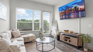 A modern living room with a sofa, a glass coffee table, a TV, and a cityscape painting. - Entire Unit Downtown Dallas, Texas - City Views near Convention center (Dallas)