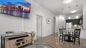 A modern living room with a flat-screen TV, a glass coffee table, and a dining area with a kitchen in the background. - Entire Unit Downtown Dallas, Texas - City Views near Convention center (Dallas)
