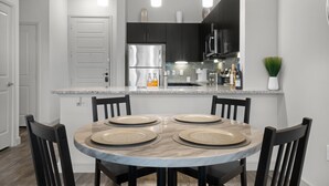A modern kitchen with a marble island, black cabinets, stainless steel appliances, and a dining area with four chairs and plates. - Entire Unit Downtown Dallas, Texas - City Views near Convention center (Dallas)