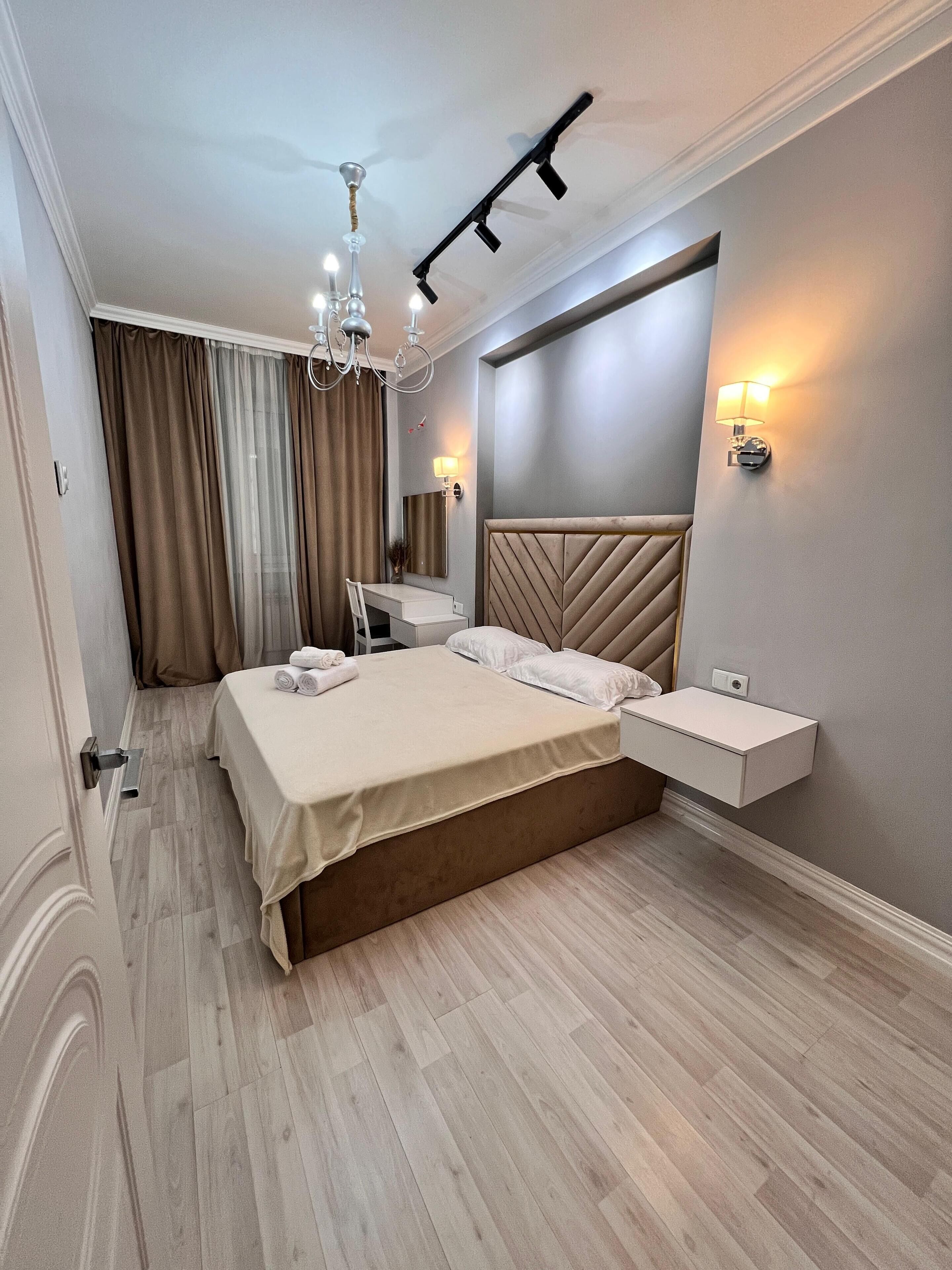 A modern bedroom with a bed, bedside table, vanity, and a chandelier.