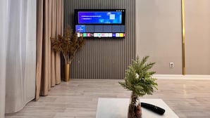 A modern living room with a flat-screen TV mounted on a wall, a white coffee table, and a potted plant. - World Retreats (Almaty)