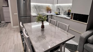 A modern kitchen with white cabinets, a stainless steel refrigerator, a marble countertop, and a dining table with chairs. - World Retreats (Almaty)