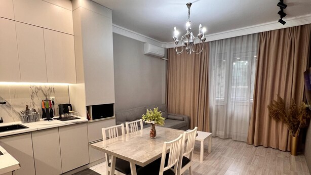 A modern kitchen with white cabinets, a marble backsplash, and a dining area with a wooden table and chairs. - World Retreats (Almaty)