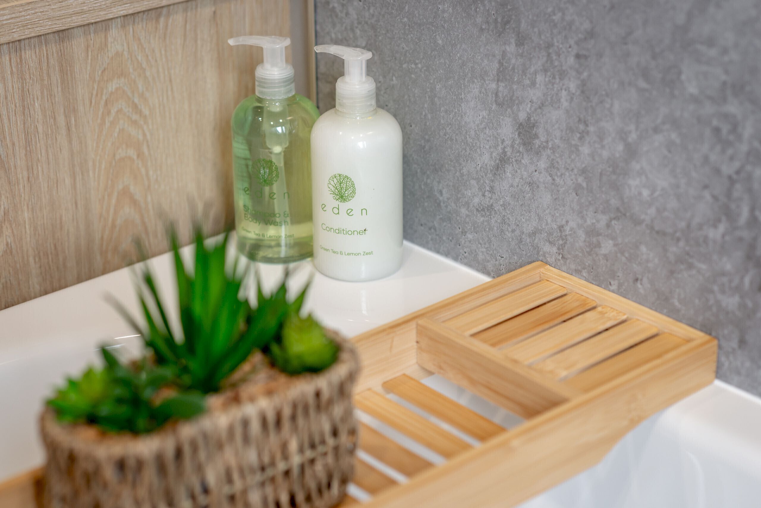Ein Badezimmer mit einem Holftablett, einer Topfpflanze und zwei Flaschen Eden Conditioner.