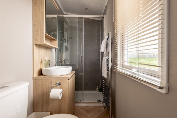 A compact bathroom with a white sink, wooden vanity, and a glass shower enclosure.