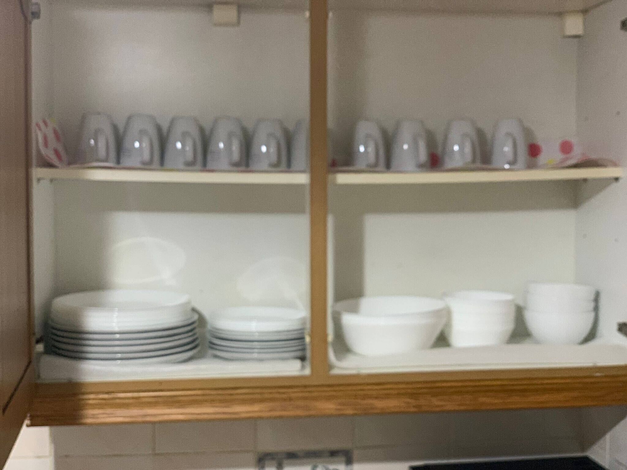 A kitchen with white cabinets and shelves holding plates, bowls, and cups.