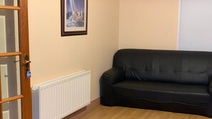 A room with a black leather sofa, a white radiator, and a wooden floor. - Room-two Rooms Total 5 Persons max (Dublin)