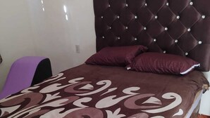 A bedroom with a tufted headboard, a patterned bedspread, and a purple chair. - Posada La escondida (San Juan del Rio)