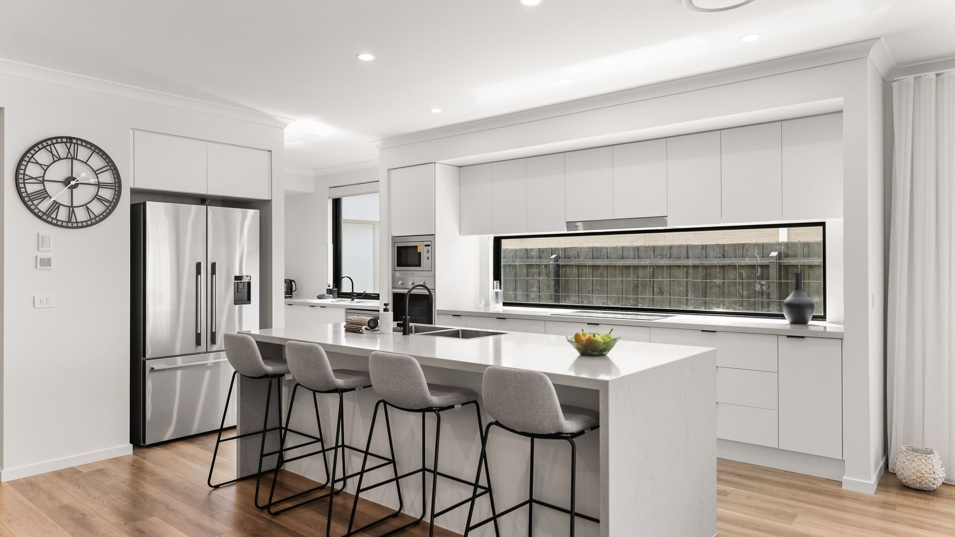 A modern kitchen with a central island, bar stools, a refrigerator, and a large window.