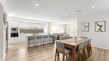 A modern kitchen with a central island, bar stools, and a dining area with a wooden table and chairs.