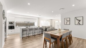 A modern kitchen with a central island, bar stools, and a dining area with a wooden table and chairs. - Our Island Home in Cowes (Cowes)