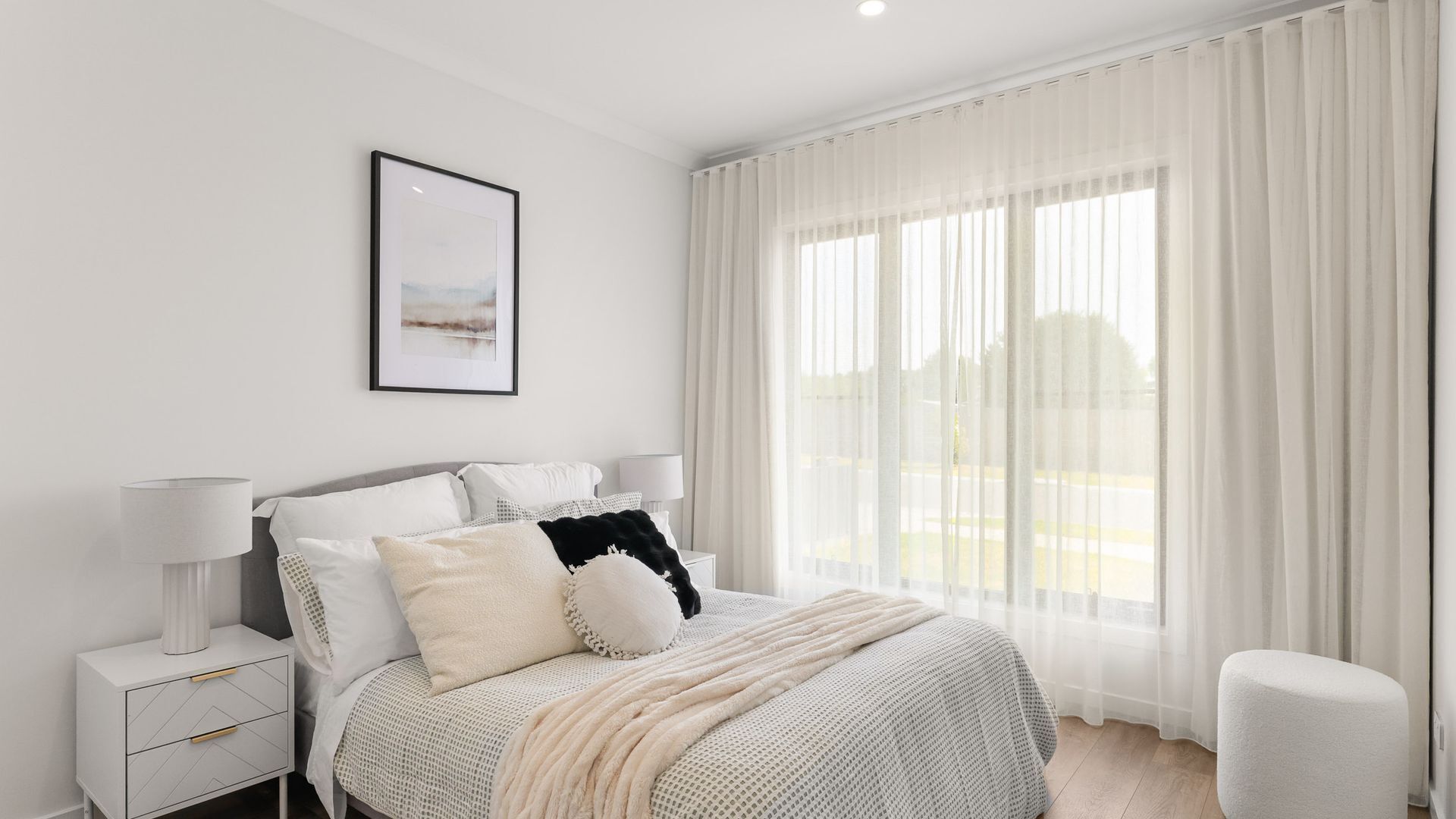 A modern bedroom with a large bed, white curtains, and a framed picture on the wall.