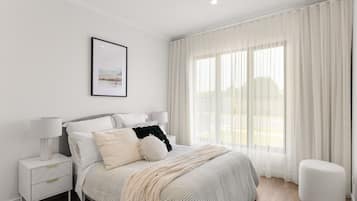 A modern bedroom with a large bed, white curtains, and a framed picture on the wall.