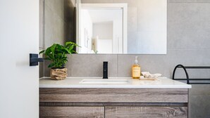 Un baño moderno con un lavabo blanco, un grifo negro, una planta en maceta, una botella de champú y una toalla.