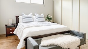 Un dormitorio ordenado con cama, mesitas de noche, lámpara y una planta en maceta.