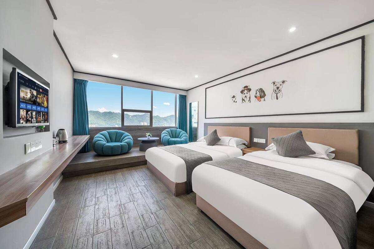 Habitación de hotel con dos camas, televisor, escritorio y un ventanal con vistas.