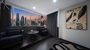 Un salon moderne avec vue sur la ville, comprenant un canapé, une table basse et un grand tableau abstrait.