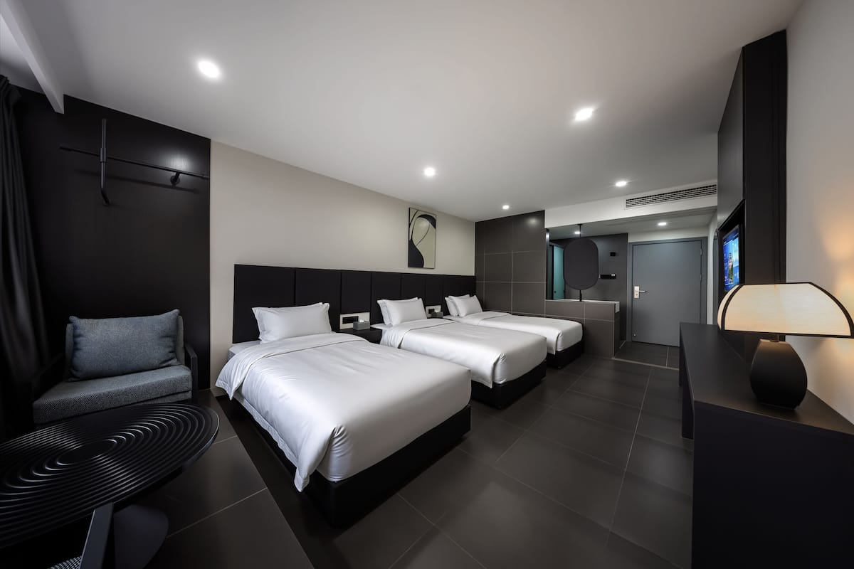Una habitación de hotel moderna con tres camas, un sofá, un escritorio y un televisor.