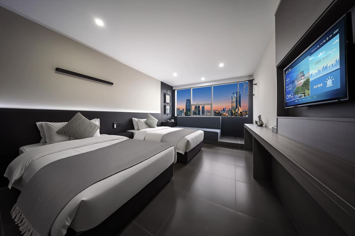 Una habitación de hotel moderna con dos camas, una tele grande y vistas a la ciudad.