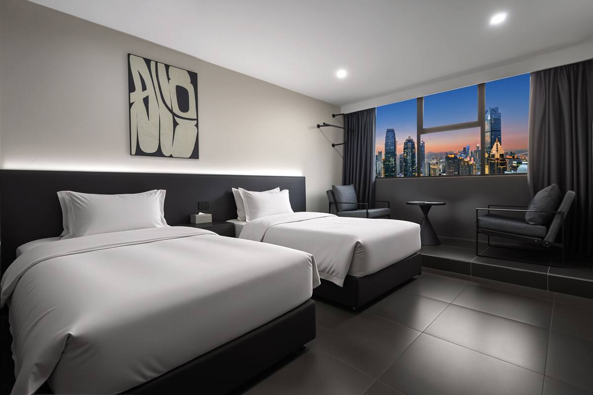 Una habitación de hotel moderna con dos camas, vistas a la ciudad, un escritorio y una silla.
