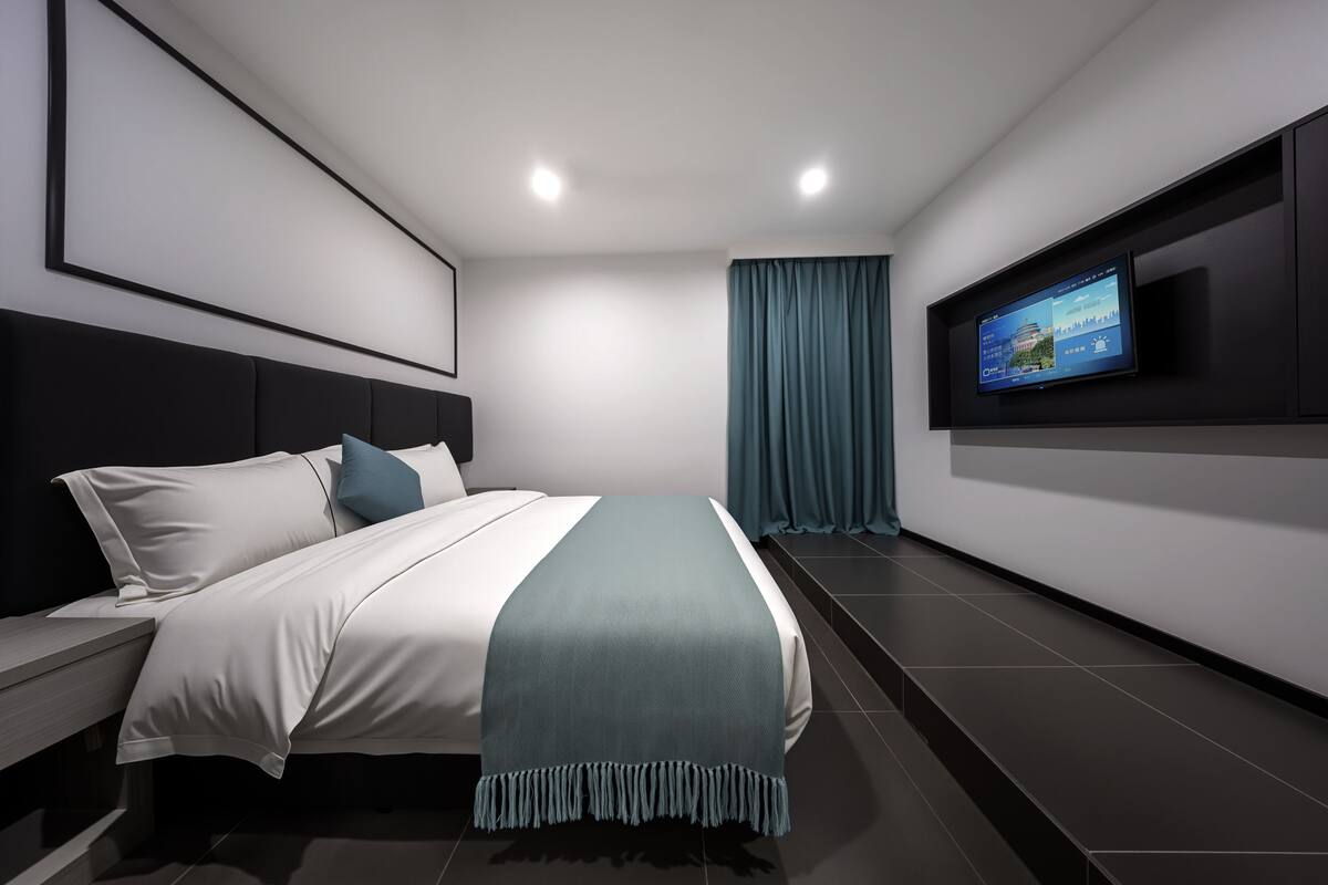 Una habitación de hotel moderna con una cama, un televisor montado en la pared y un gran ventanal con cortinas.