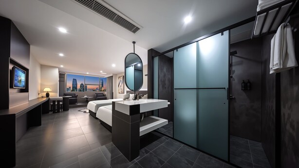 Une chambre d’hôtel moderne équipée d’un lit, d’un bureau, d’un grand miroir, d’une salle de bain avec douche et offrant une vue sur la ville.