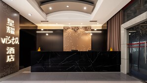 Un espace d’accueil d’hôtel au design moderne, comprenant un comptoir de réception en marbre, un mur avec un panneau lumineux et une grande fenêtre offrant une vue panoramique.