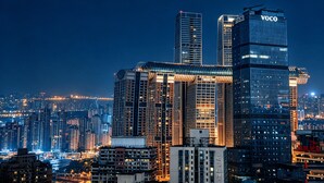 Un immeuble de grande hauteur, sur lequel on peut voir un grand panneau « VOCO », entouré d’autres bâtiments imposants dans un paysage urbain nocturne.