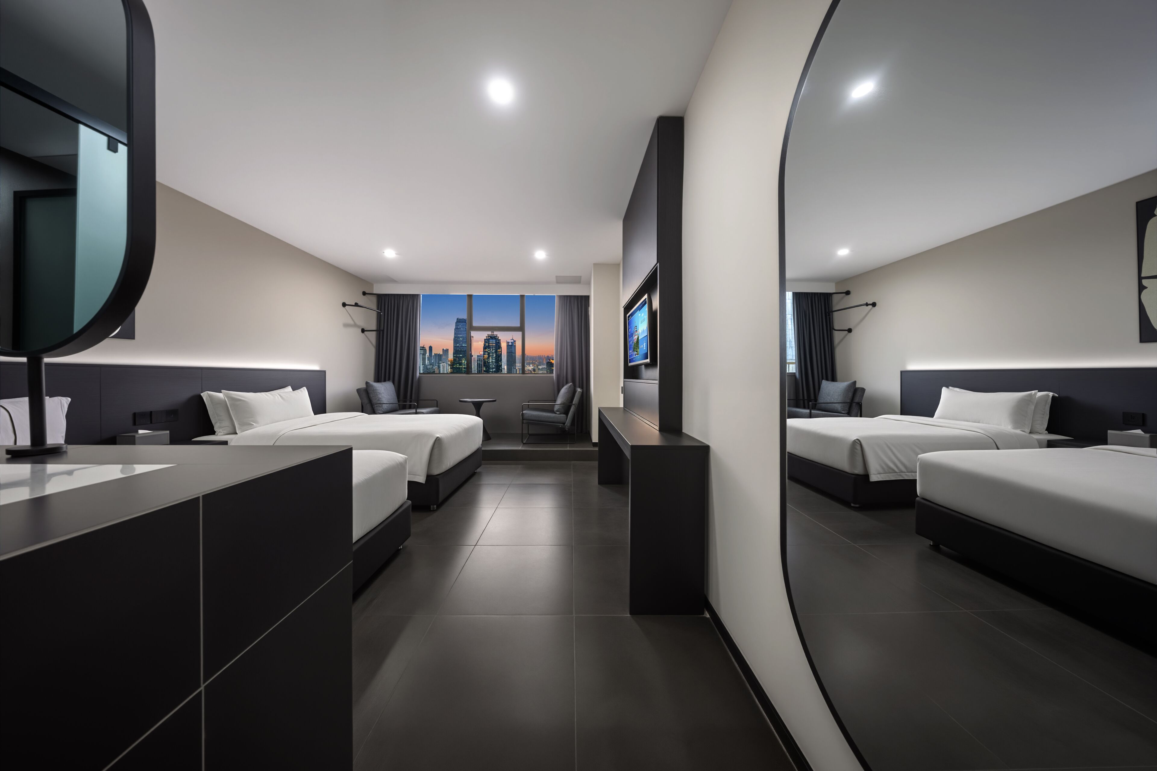 A modern hotel room with two beds, a large mirror, a TV, and a city view.
