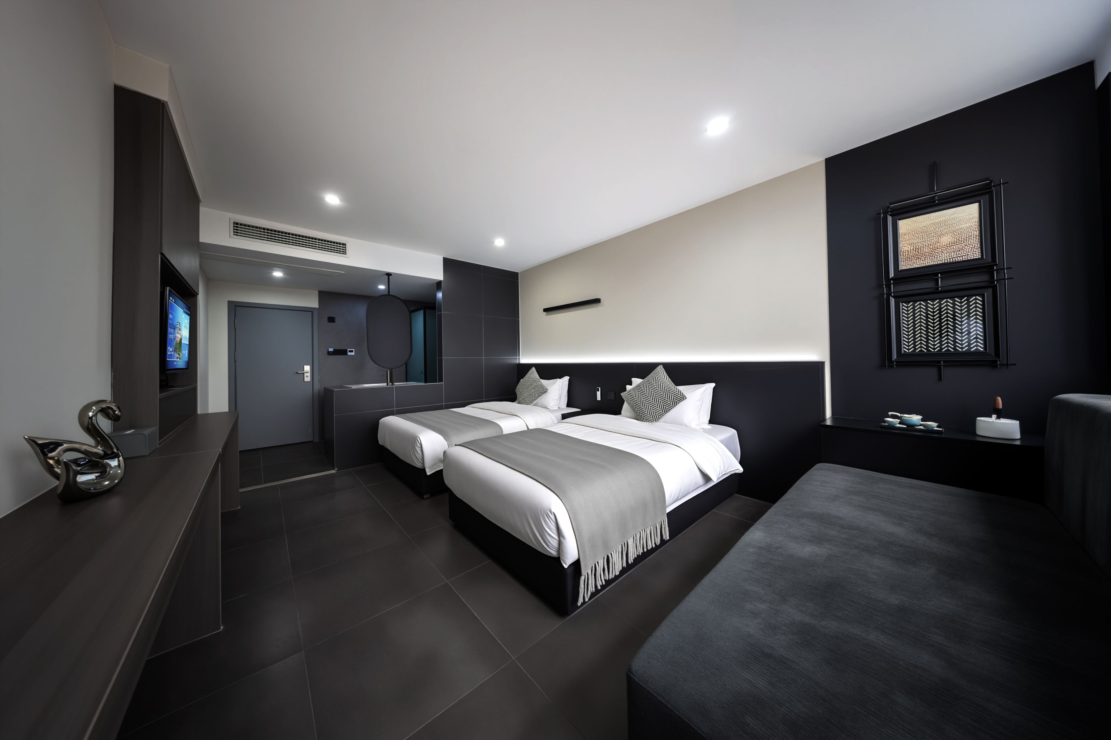 Ein modernes Hotelzimmer mit zwei Betten, einem Fernseher, einem großen Spiegel und einer Wand in dunklen Tönen.