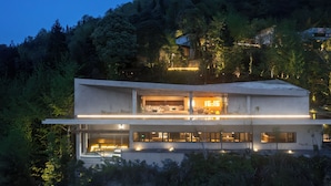 A modern two-story building with large windows and a flat roof, surrounded by dense forest. - The Mountain Route (Guang'an)