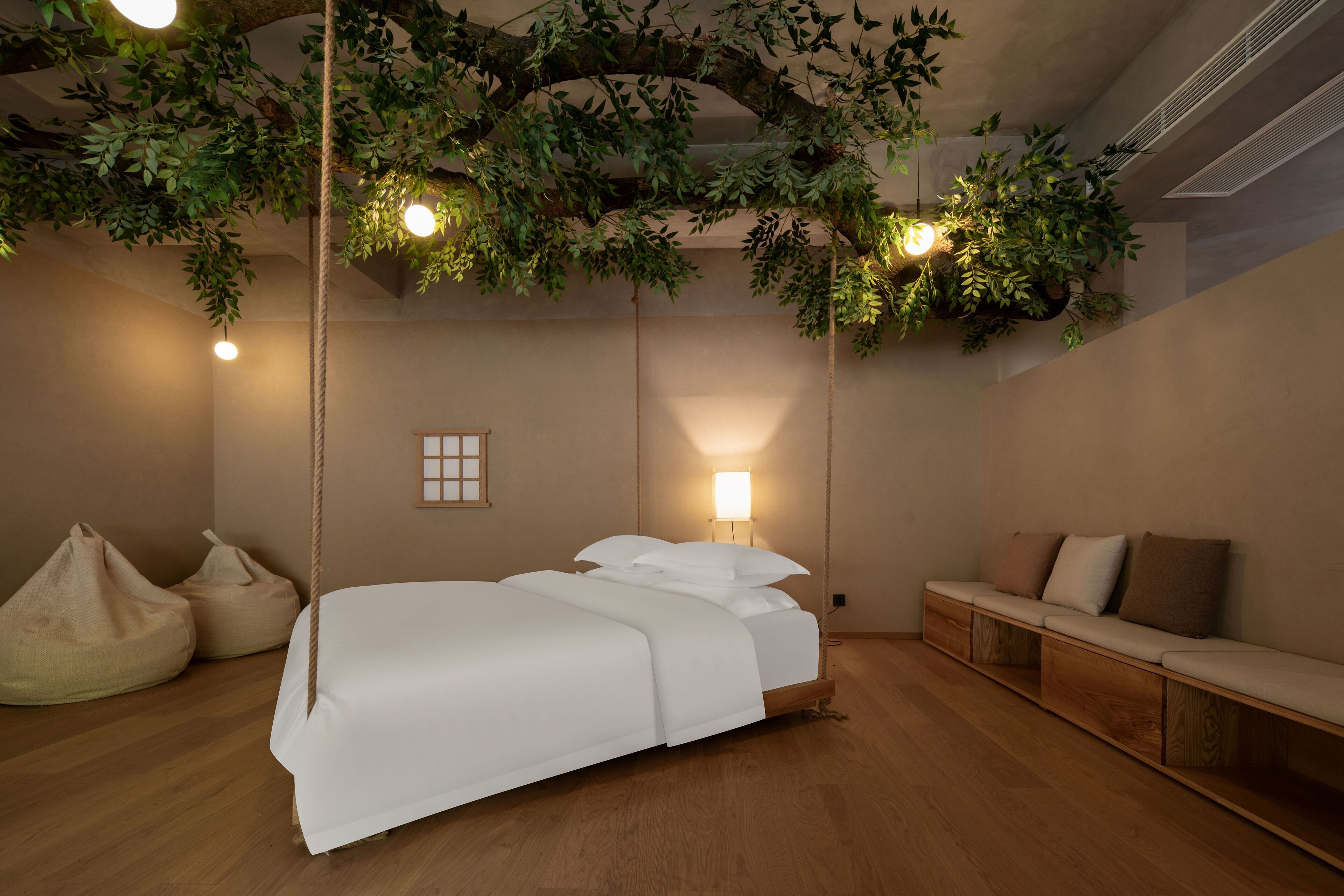 A bedroom with a bed, a bench, and hanging plants.