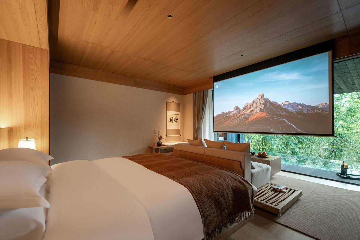 A modern bedroom with a large bed, a TV, and a view of mountains through a window.
